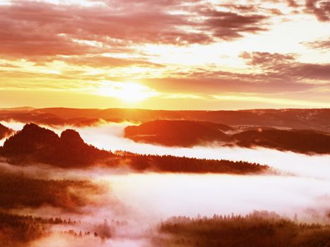 Red filter photo. Red daybreak. Misty daybreak in a beautiful hills. Peaks of hills are sticking out from foggy background, the fog is red and orange due to Sun rays. 