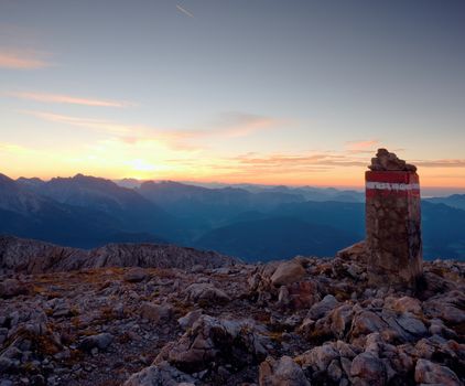 Border stone on Apine gravel  cliff. Austria Germany border. Daybreak horizon above blue foggy valley. Mountains increased from humidity