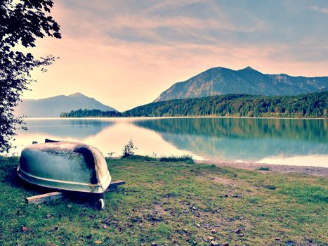 Upside down  fishing paddle boat on bank of Alps lake. Morning autumnal lake. Dramatic and picturesque scene. Mountains in water mirror.