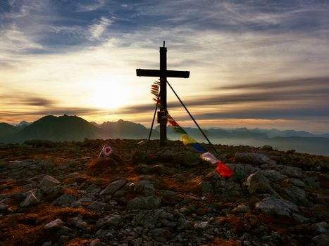 Big wooden cross at mountain peak in wind with Buddhist praying flags.  Cross on top of a mountains peak as typical in the Alps. Monument to the dead climbers