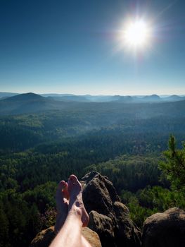 Naked male hairy legs take a rest on peak of rock. Outdoor activities in summer weather. Long forest valley in hilly landscae of nature park.