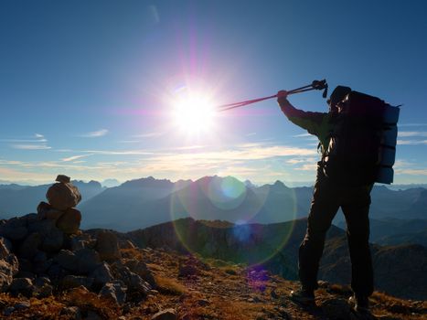 Lens flare light, strong defect. Tall backpacker with poles in hand. Sunny weather in rocky mountains. Hiker with big backpack stand on rocky view point above misty valley. 