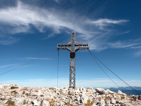 Steel cross raised  at mountain summit  in Alps. Sharp peak. Daybreak Sun in sky. Steel crucifix in memory of victims of mountains.