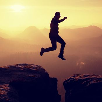 Young crazy man jump on mountain peak. Silhouette of jumping man and beautiful sunset sky. Vintage effect, lens defect.