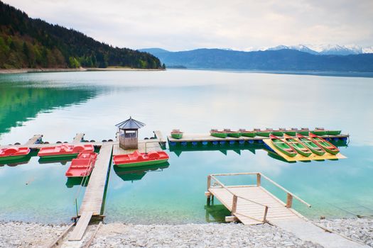 Empty wooden wharf mole. Blue Alps lake with Rental rowing boats in marina. Wharf for trip ships.