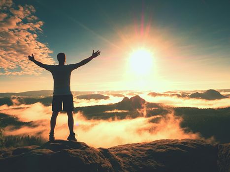 Happy man gesture of triumph with rams in air. Funny hiker on peak of sandstone rock in national park Saxony Switzerland watching to horizon