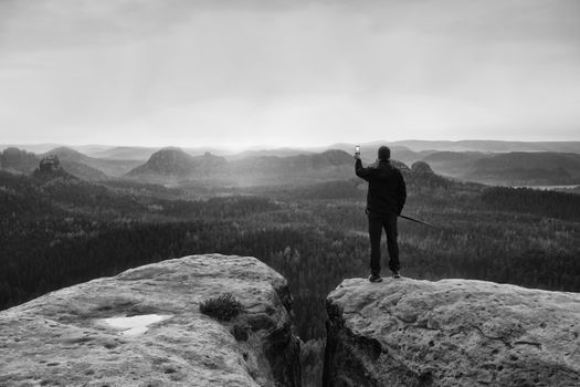 Hiker stand with smart phone on top of mountain and enjoying spring sunrise. Tourist guide with trekking poles.