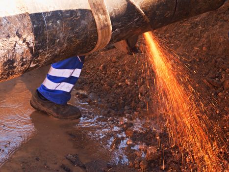 Man works, big pipe cutting with electric spiral machine. Hor sparks flying away from cut place.