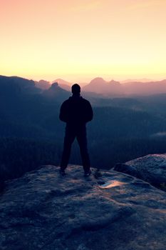 Tall man in black on cliff and watch to mountain sunrise.Silhouette in selfconfident pose.  Dark silhouette of rocks.