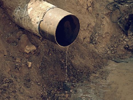 Rusty Old Iron Pipe With Clear Water Flowing From It. Waste water drain pipe in clay