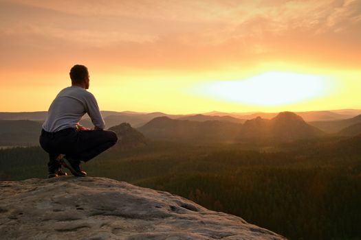 Hiker in black sit alone on the rock summit. Wonderful daybreak in mountains, heavy mist in deep valley. Man sit on the rock.