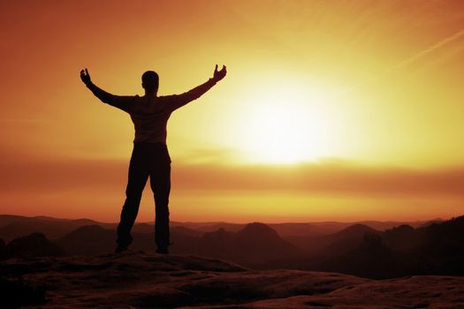 Happy man gesture of triumph with rams in  air. Funny hiker on peak of sandstone rock in national park Saxony Switzerland watching to horizon