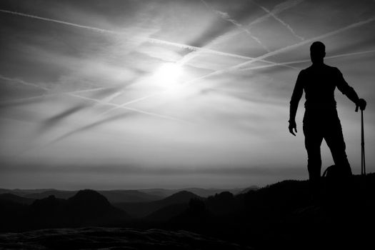 Tourist with poles in hands stand on rock watching  for next step. Sunny spring daybreak in mountains.Vignetting effect.. 