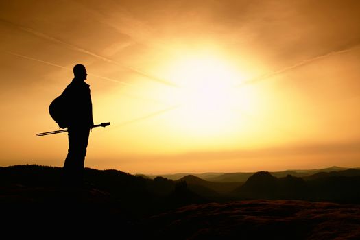 Man hiker in the mountains for a walk in the evening with trekking poles. Spring foggy valley in mountains