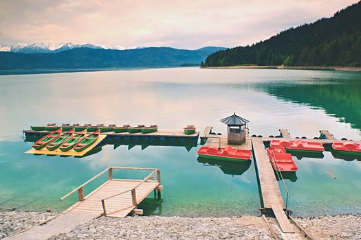Empty wooden wharf mole. Blue Alps lake with Rental rowing boats in marina. Wharf for trip ships.