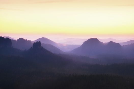 Tourist resort. Fantastic dreamy sunrise on the top of the rocky mountain with the view into misty valley. Vivid dreamy effect.