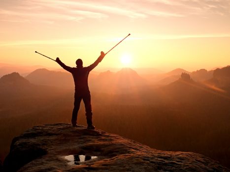 Hiker with  medicine crutch above head achieved mountain peak. Broken leg fixed in immobilizer Deep misty valley bellow silhouette of man with hand in air. Spring daybreak