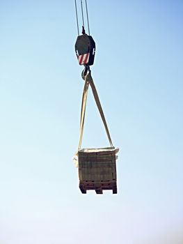 Crane Hook with Stacked white bricks on a wooden Pallet, clear blue sky in the background