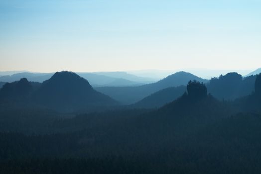 Sunrise in a beautiful mountain of Czech-Saxony Switzerland. Sandstone peaks increased from foggy background, the fog is orange due to sun rays. 
