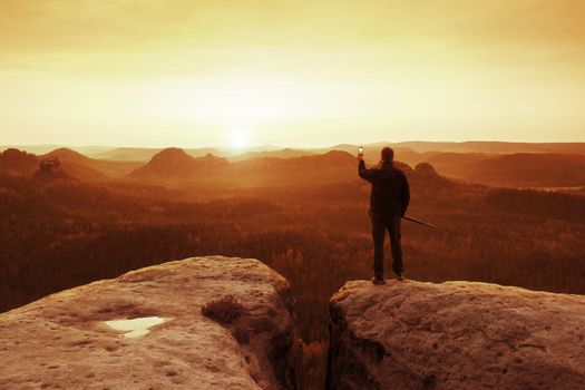 Hiker is taking photo by smart phone on the peak of mountain at sunrise. Red vintage effect.