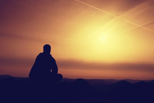  Hiker in black sit alone on the rock summit. Wonderful daybreak in mountains, heavy mist in deep valley. Man sit on the rock.