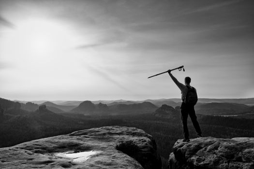 Tourist with poles in hands stand on rock watching  for next step. Sunny spring daybreak in mountains.Vignetting effect.. 