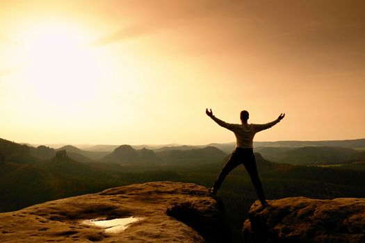 Summit achievemnt. Hiker in black celebrate triumph between two rocky peaks. Wonderful daybreak in rocky mountains, heavy orange mist in deep valley