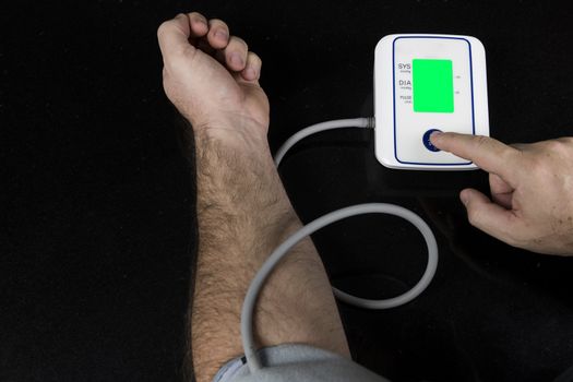 Man measuring his blood pressure at home with an automatic blood pressure monitor. Picture of the machine and arm of the person with a finger pressing the srart button