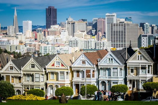 San Francisco, California, United States, November 2013: View on the Painted Ladies Victorian houses of San Francisco with cityscape and skyline in the background on a blue sky. People sitting front