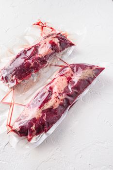 Pair of chuck roll beef steak, vacuum packed organic meat for sous vide cooking on white concrete textured background, side view