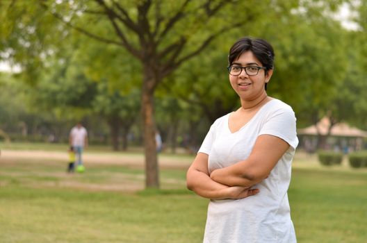 Smart Indian woman standing, posing for the camera with hands crossed / folded in a park wearing white in summers in New Delhi, India