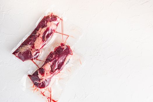 Pair of chuck roll beef steak, vacuum packed organic meat for sous vide cooking on white concrete textured background, top view space for text