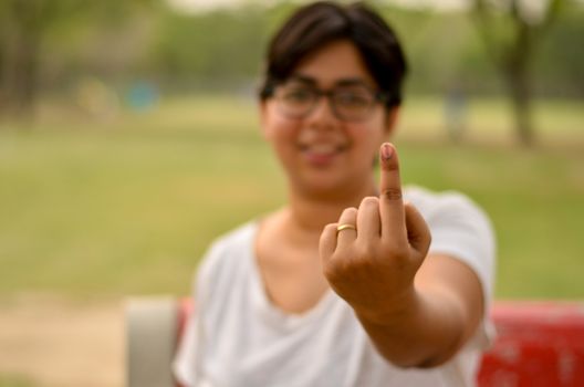 Young Indian woman sitting on the red bench in a park and showing their inked finger after casting their vote in Indian assembly election in New Delhi, India