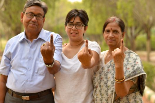 Happy Family portrait - Senior Retired parents and their daughter showing the inked finger after voting in Indian elections in an outdoor park. Celebrating world's largest democratic elections concept