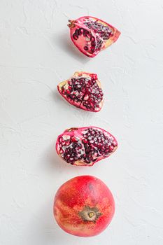 Cuts of pomegranate and whole garnet over white background, top view