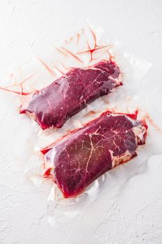 Set of vacuum packed organic beef meat rump steak on white concrete textured background, side view