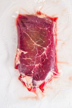 Vacuum packed organic beef meat rump steak on white concrete textured background, top view space for text.