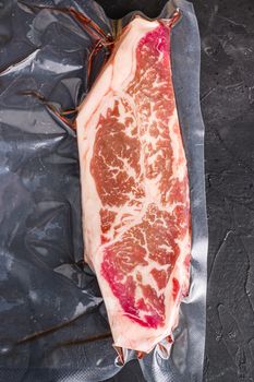 Top blade steak, vacuum packed organic beef for sous vide cooking on black textured background, top view