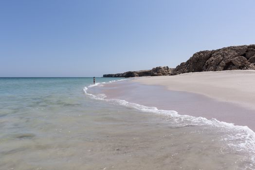 Woman alone at a wild Beach of Ras Al Jinz and going to swim in the ocean (Gulf of Oman), Oman, Sultanate of Oman. It is close to Ras Al Hadd and many turtles are coming in the region to nest