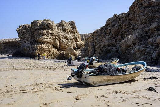 Fishermen arranging their net on the beach of Ras Al Jinz besides some boats, Oman