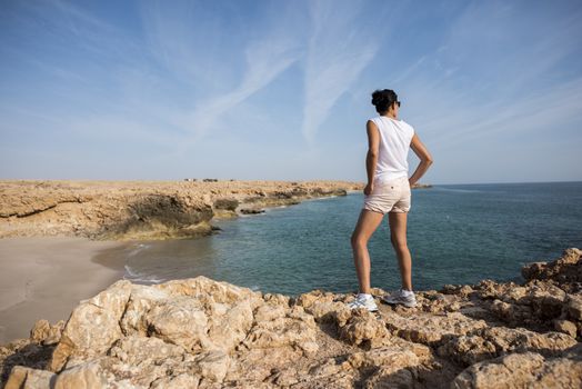 Woman admiring the wild coast of Ras Al Jinz with a sandy beach at her left, Oman