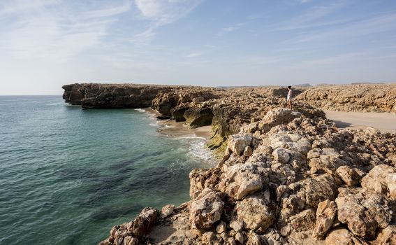 Woman admiring the wild coast of Ras Al Jinz with a sandy beach at her left, Oman