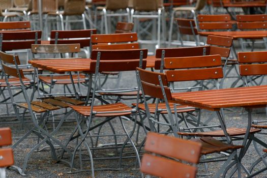 Unoccupied chairs and tables in a garden restaurant with table legs and chair legs made of iron and wooden tops, Germany