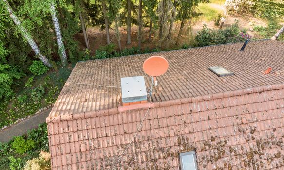 Overflight of the roof of a detached house to check the condition of the satellite antenna for the reception of television and Internet, aerial view made with drone