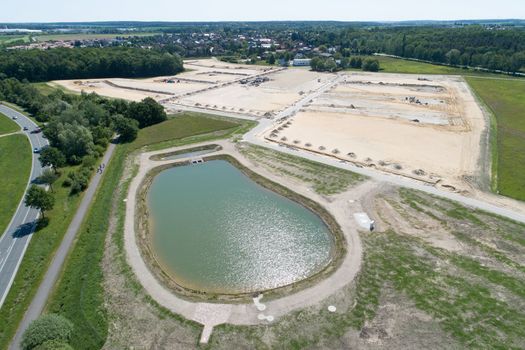 Aerial view from a rainwater basin and a new development area on sandy ground with the planum for new houses, taken at an angle, great height