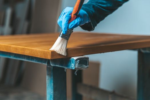 coating of wooden surface with protective varnish. hand in blue rubber glove uses brush.