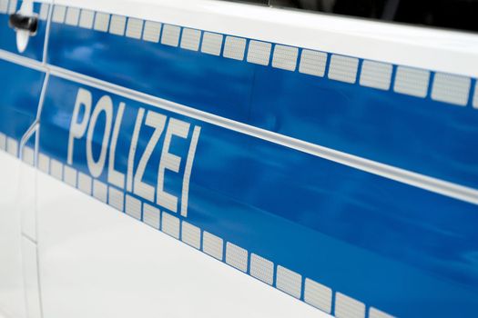 Inscription "Police" in white luminous colour on a blue background on the side of a police car, Germany
