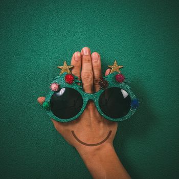 Christmas glasses that decoration with Christmas tree and red ball on hand on green background