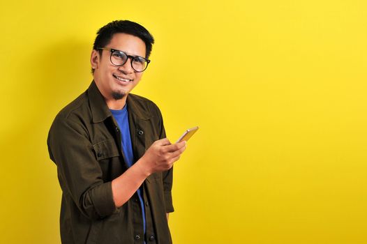 Portrait of happy smiling Asian man using smartphone wearing casual t-shirt and jacket with eyesglasses, get the best price, using simple mobile banking payment
