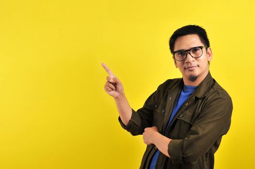 Handsome of happy smiling asian man pointing of a copyspace, isolated on yellow background